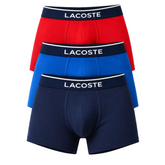 Three pairs of Lacoste men's boxer briefs stacked vertically, showing the red, blue, and navy blue options. Each pair features a dark navy elastic waistband with the brand name 'LACOSTE' printed in white capital letters.