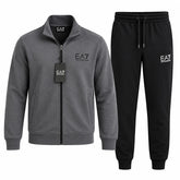 A two-piece men's loungewear set by EA7, featuring a heather gray zip-up jacket with a black zipper and a black hangtag, paired with black sweatpants with a white EA7 logo on the left thigh.