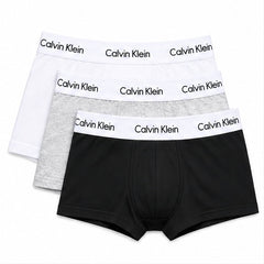 Three pairs of Calvin Klein men's boxer briefs stacked together on a white background, featuring black, light gray, and white fabrics with white waistbands printed with the Calvin Klein brand name.