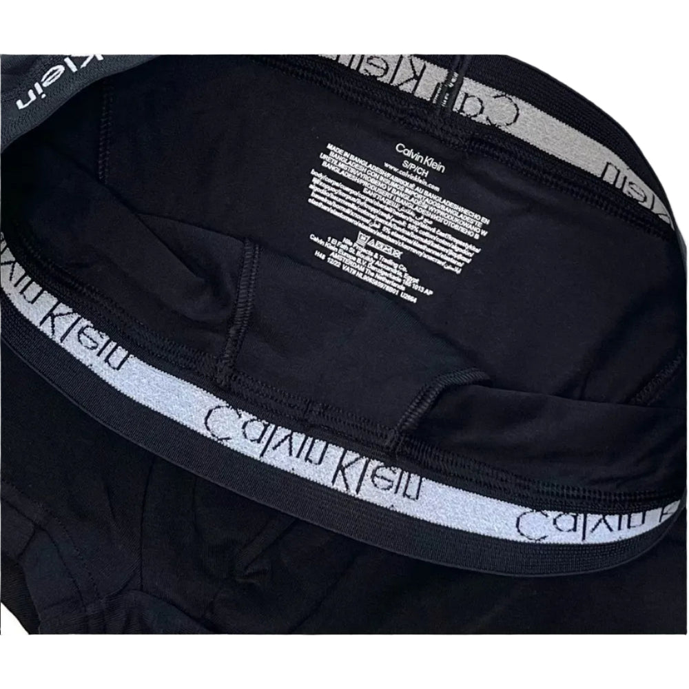 Close-up of black Calvin Klein briefs showing the inner waistband with the signature gray and black logo tape and white brand text.