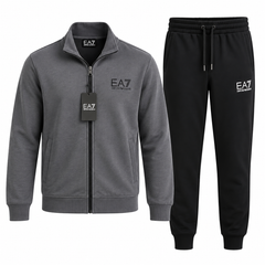 A two-piece men's loungewear set by EA7, featuring a heather gray zip-up jacket with a black zipper and a black hangtag, paired with black sweatpants with a white EA7 logo on the left thigh.