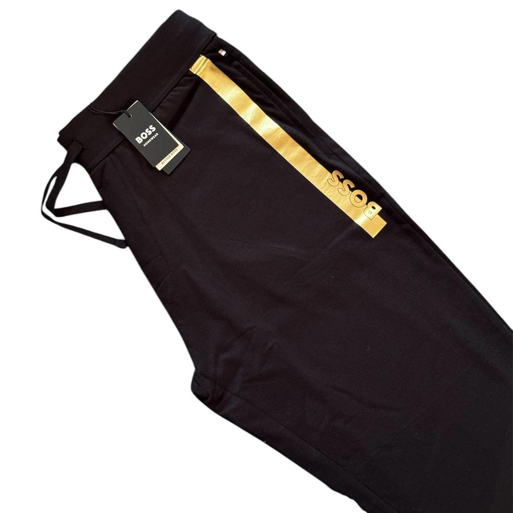 Black HUGO pants with a prominent gold metallic stripe and logo on the side, shown with a black hangtag on a white background.
