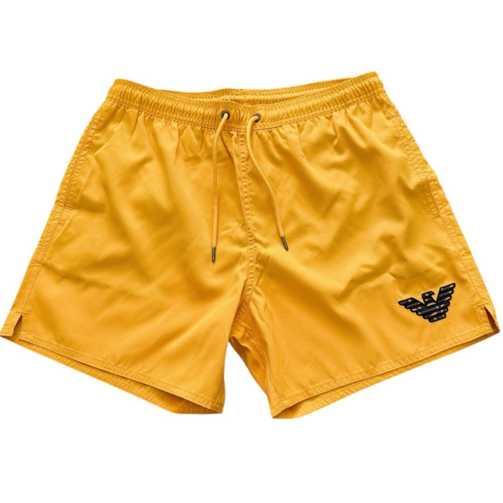 Yellow Emporio Armani swim shorts with a black embroidered eagle logo on the lower left leg, featuring an elastic waistband and drawstring.