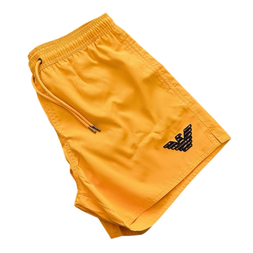 Yellow athletic shorts with a black embroidered logo on the lower left leg, featuring an elastic waistband and drawstring.