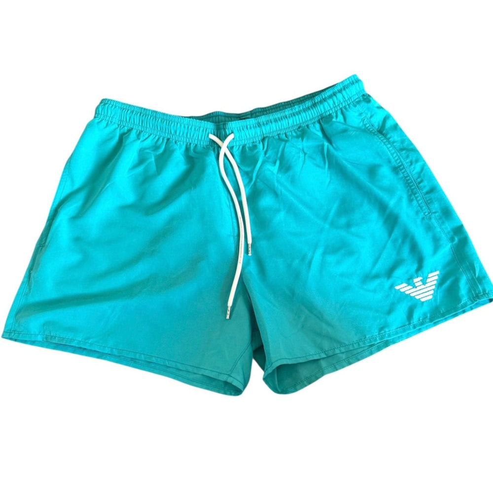 Turquoise blue swim shorts with a white drawstring and a white embroidered eagle logo on the lower left leg, displayed flat against a white background.