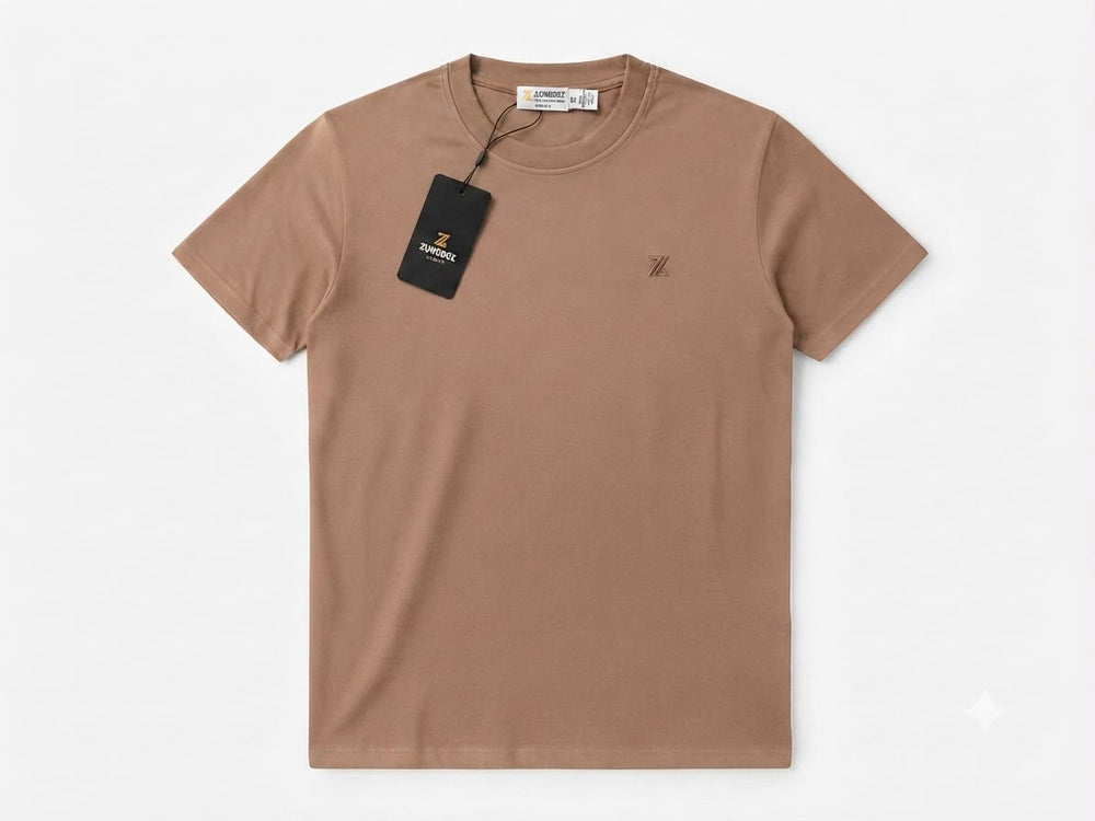 A short-sleeve crewneck t-shirt in a muted tan-brown color, featuring a small embroidered logo on the left chest and a black hangtag attached to the collar, displayed on a clean white background.