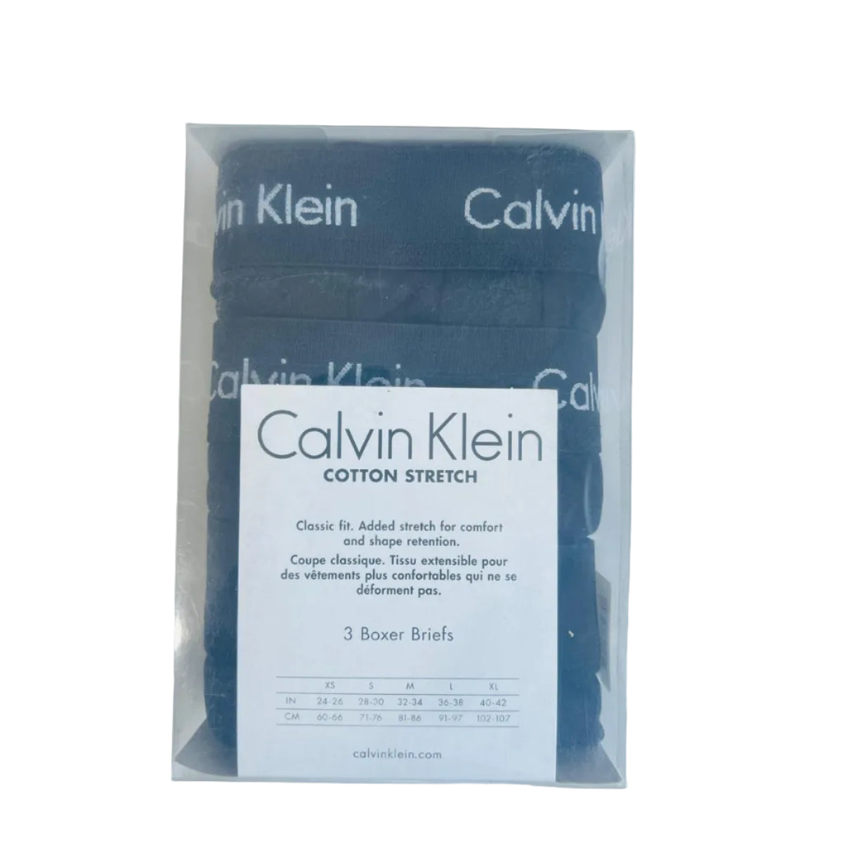Pack of Calvin Klein cotton stretch boxer briefs in a clear plastic sleeve with a white size card, placed on a light wood surface next to a black keyboard.