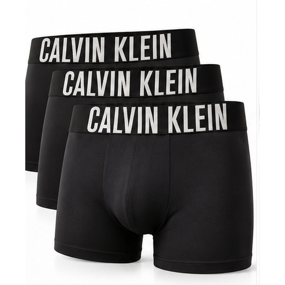 Three pairs of black Calvin Klein boxer briefs arranged in a staggered stack, each with a wide black waistband featuring the brand name 'CALVIN KLEIN' in bold white capital letters, set against a plain white background.